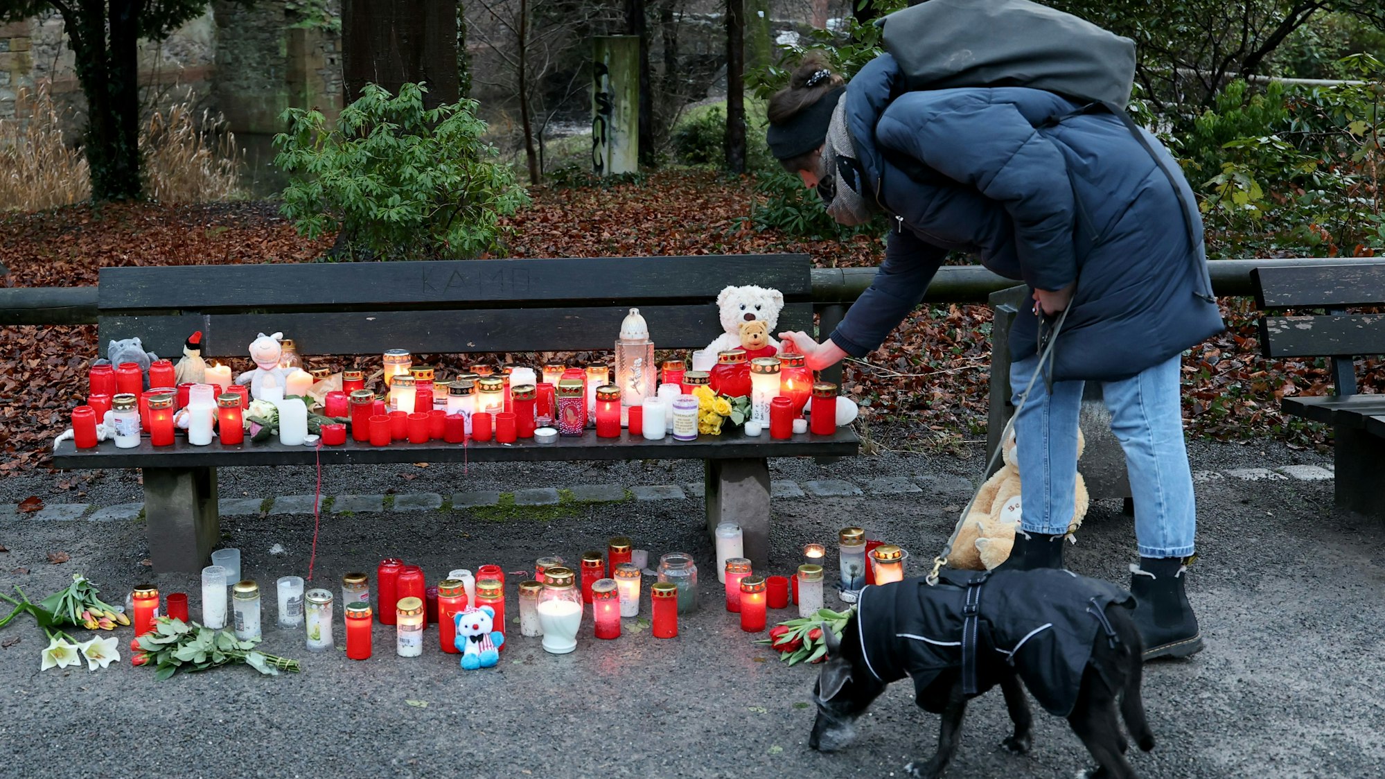 Eine Frau stellt eine Trauerkerze neben Blumen und Kuscheltieren nach dem tödlichen Angriff in einem Park am Tatort auf einer Bank ab.