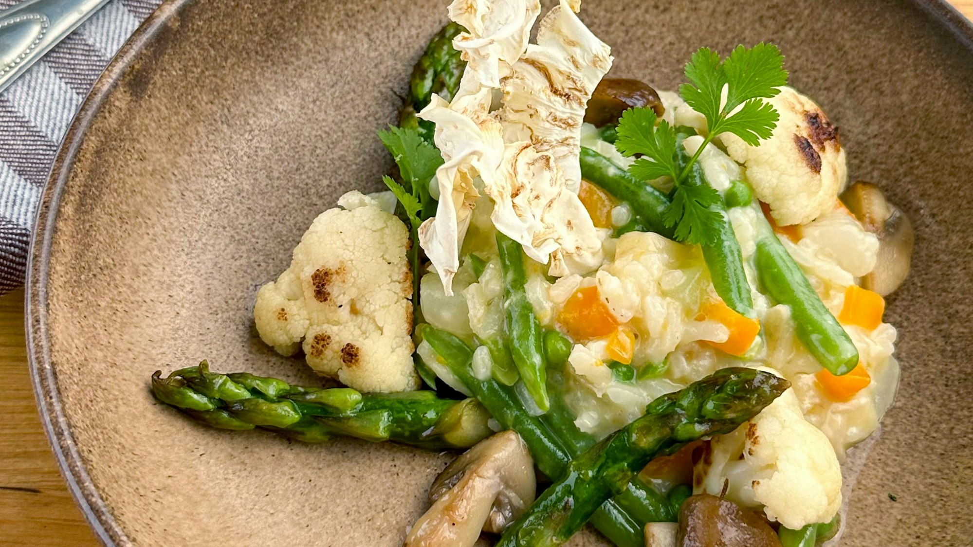 Bei Jörg Färber gibt es Leipziger Allerlei auch als Risotto mit Sellerie-Chips, hier auf einem braunen Teller. Foto nur zur redaktionellen Verwendung im Zusammenhang mit dem genannten Text und nur bei vollständiger Nennung des vorstehenden Credits.