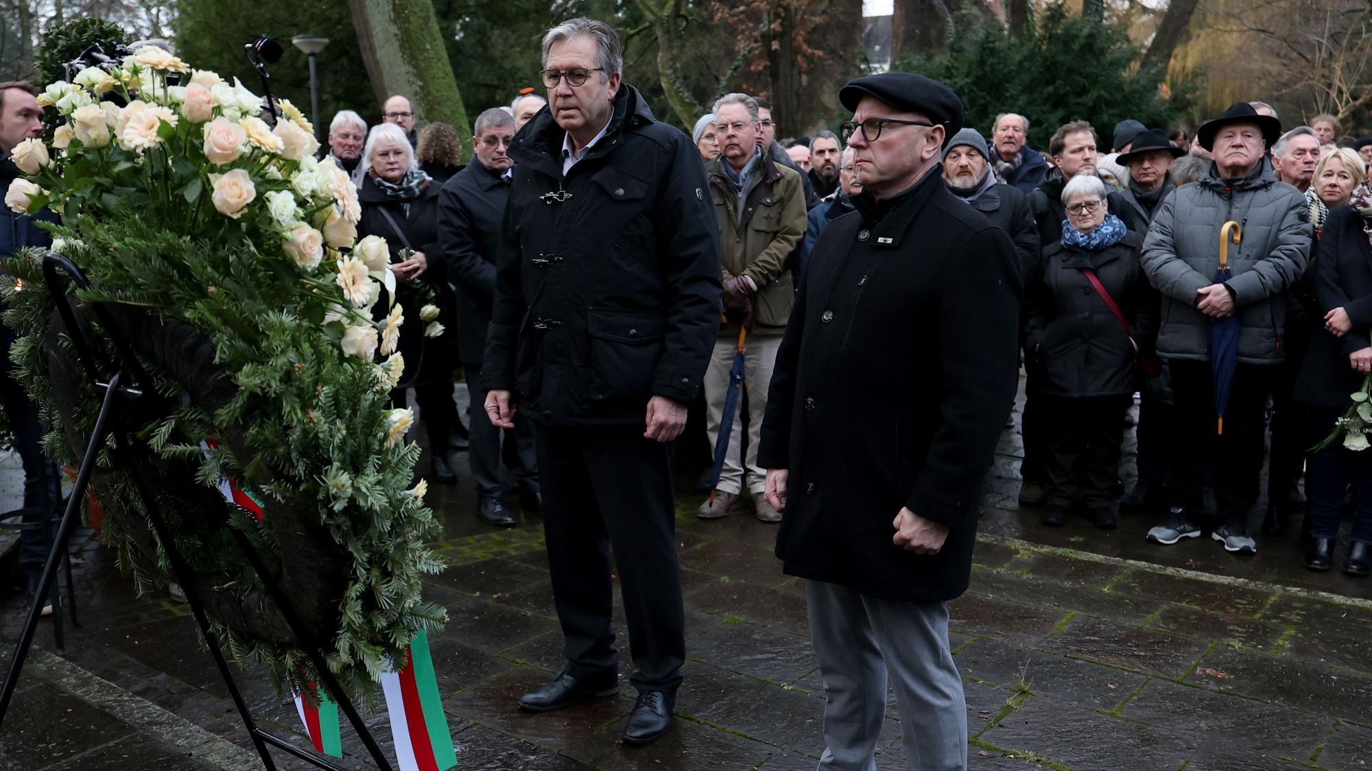 Der Aschaffenburger Oberbürgermeister steht in schwarz vor einem großen Blumenkranz.