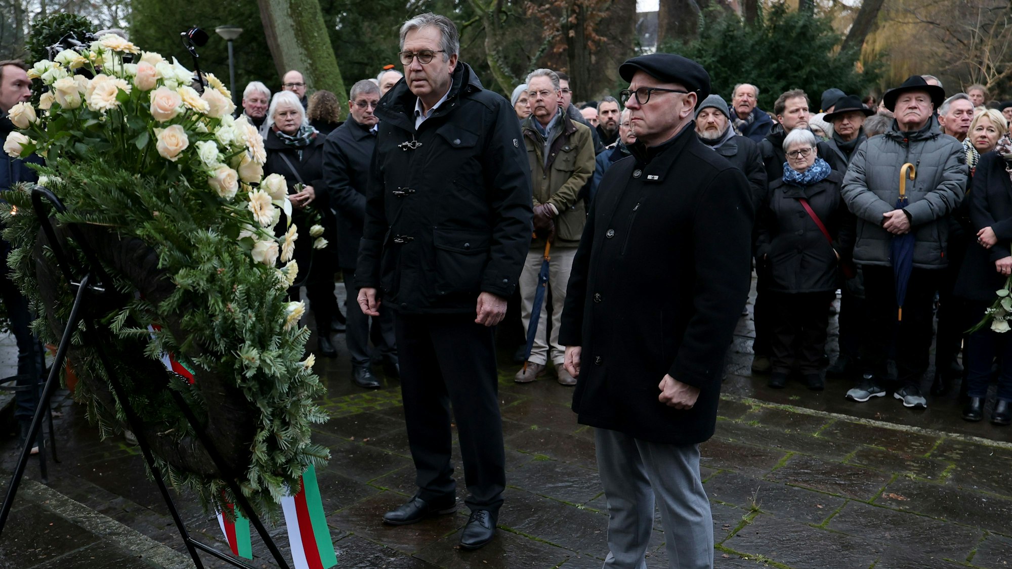 Der Aschaffenburger Oberbürgermeister steht in schwarz vor einem großen Blumenkranz.