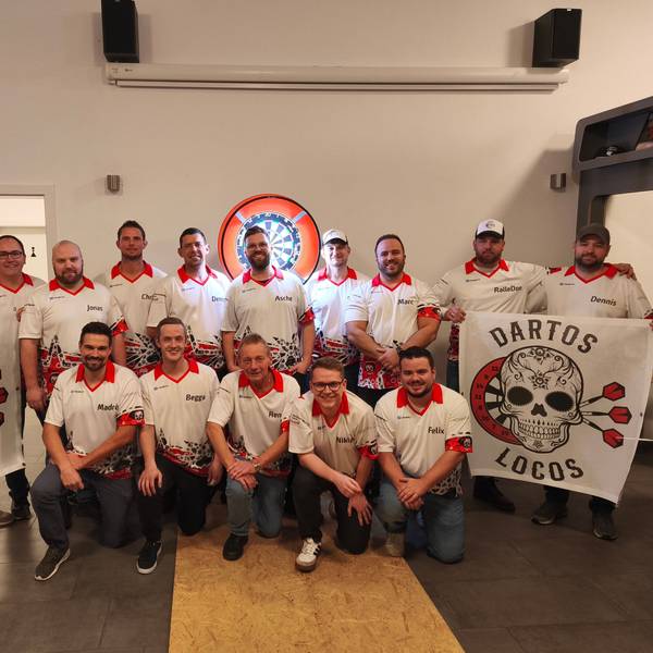 Die Spieler der Dartos Locos aus Billig posieren für die Kamera, links und rechts halten sie Fahnen mit dem Teamlogo hoch. Im Hintergrund ist eine beleuchtete Darts-Scheibe zu erkennen.