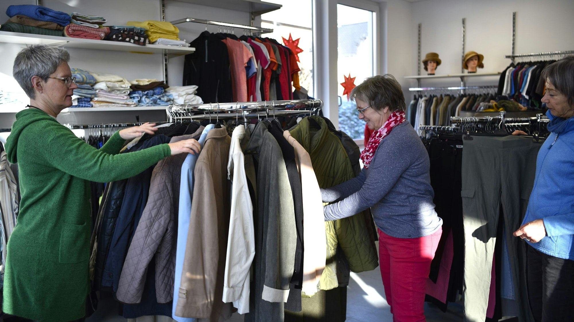 Astrid Franzen (v.l.), Marlies Wingartz und Margret Arbach hängen Jacken und Mäntel auf einen Kleiderständer.