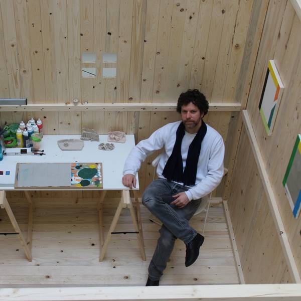 Auf dem Bild ist ein Künstler in einem Atelier aus einem Holzkubus zu sehen.