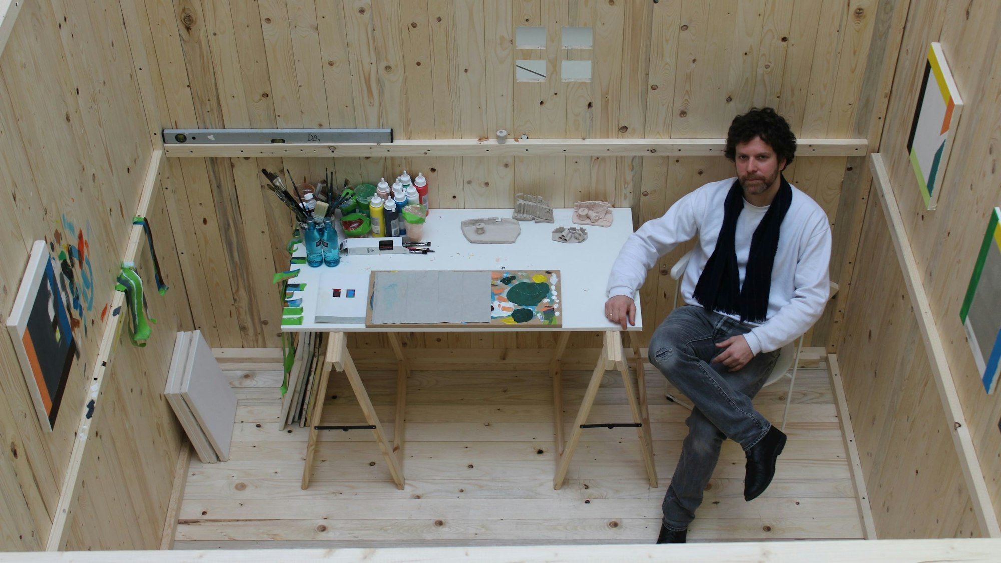 Auf dem Bild ist ein Künstler in einem Atelier aus einem Holzkubus zu sehen.