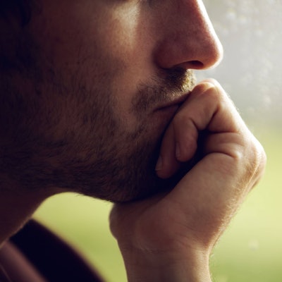 Mann stützt sein Kinn auf seine Hand und schaut aus dem Fenster.