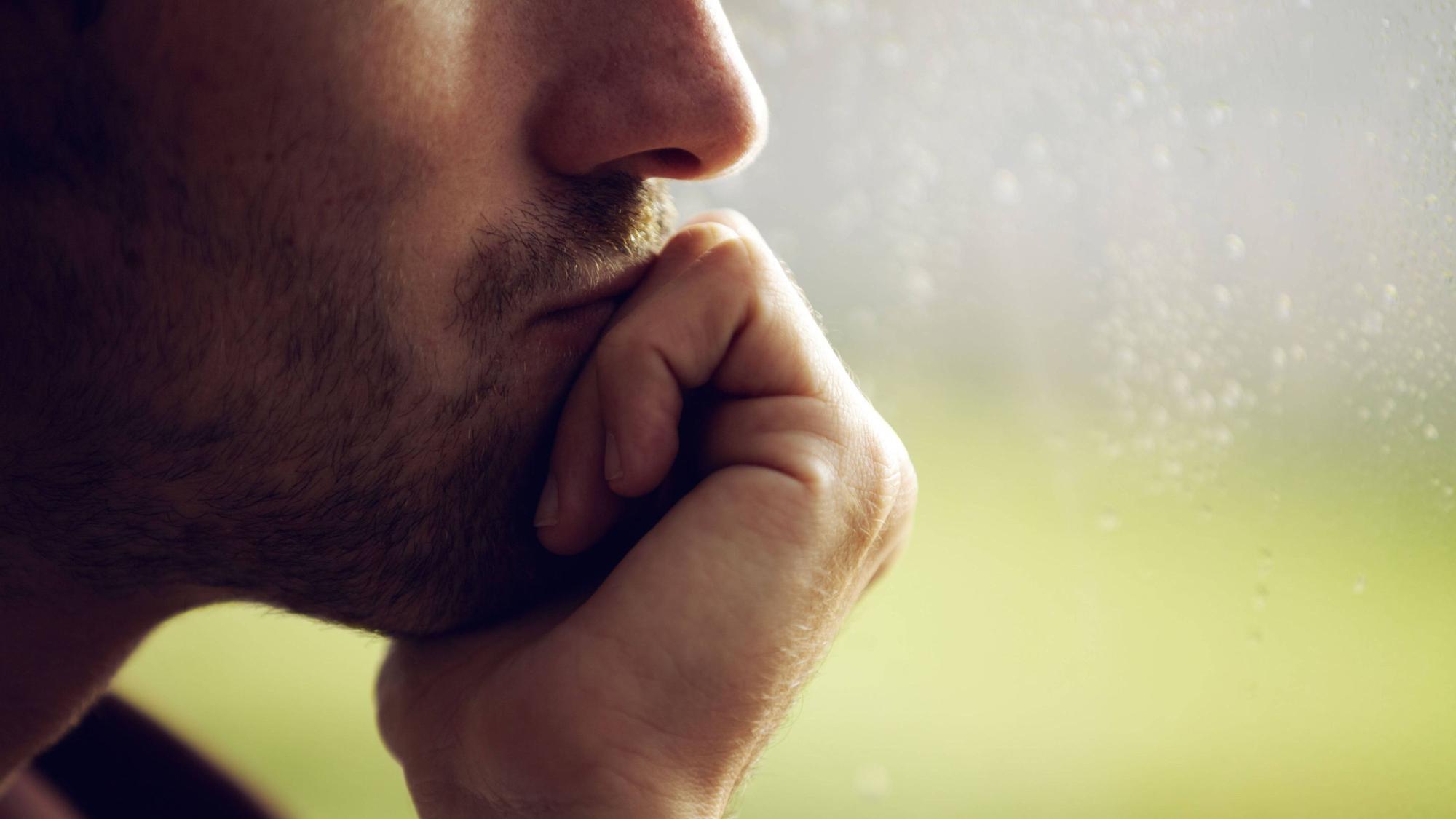 Mann stützt sein Kinn auf seine Hand und schaut aus dem Fenster.