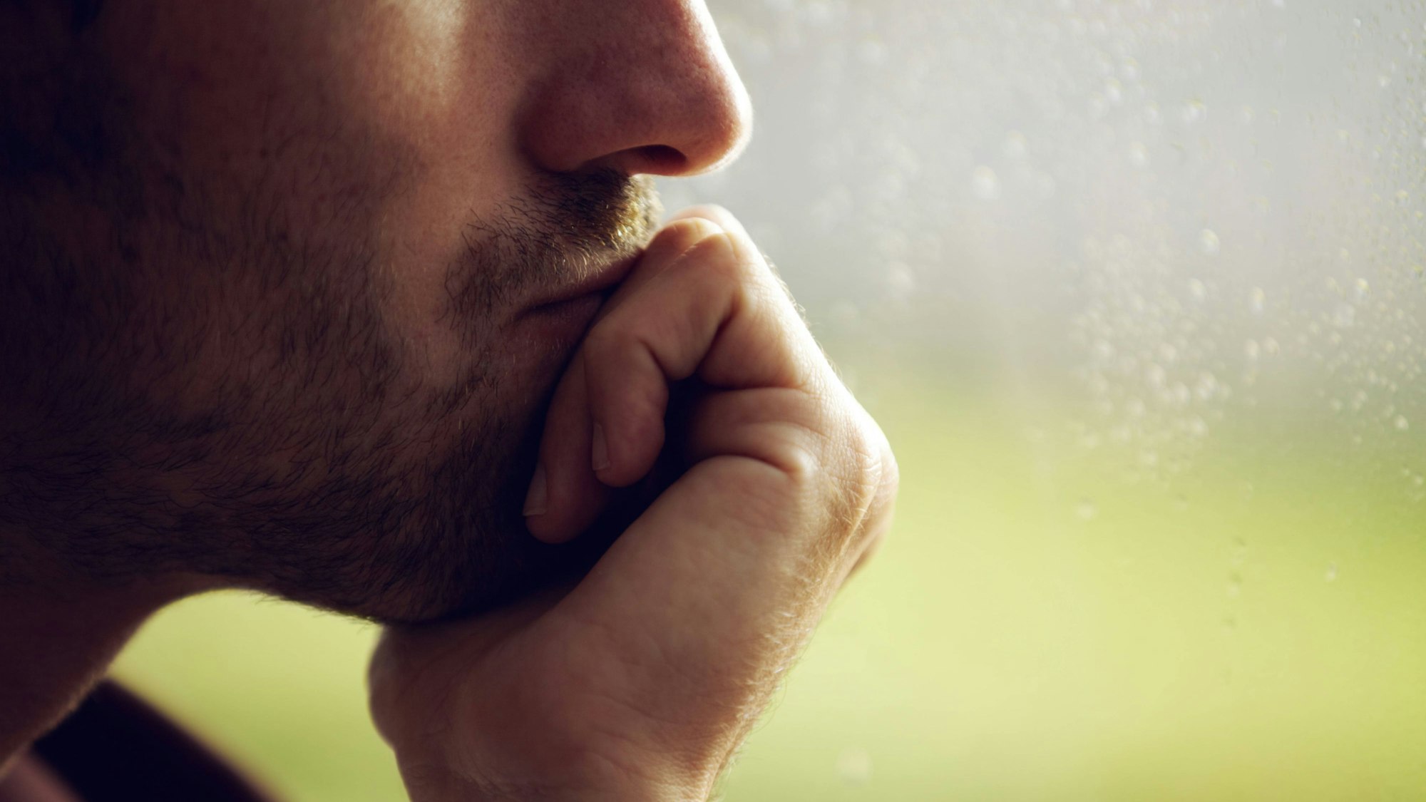Mann stützt sein Kinn auf seine Hand und schaut aus dem Fenster.