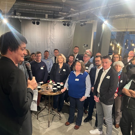 Ein Mann steht als Redner auf einer Bühne vor Publikum.