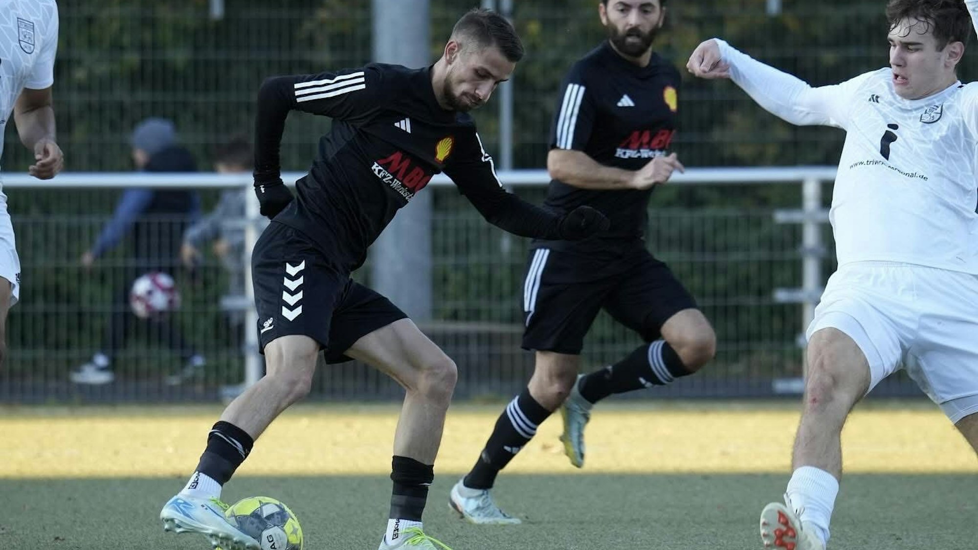 Das Bild zeigt Fußballer in schwarzer Kleidung, der sich mit dem Ball am Fuß an seinem Gegenspieler vorbei dribbelt.