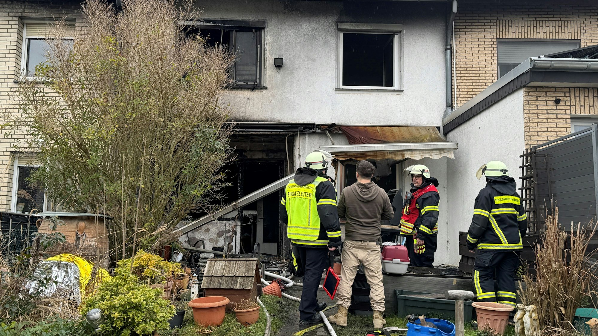 Das Foto zeigt Einsatzkräfte der Feuerwehr im Garten vor dem zerstörten Haus.
