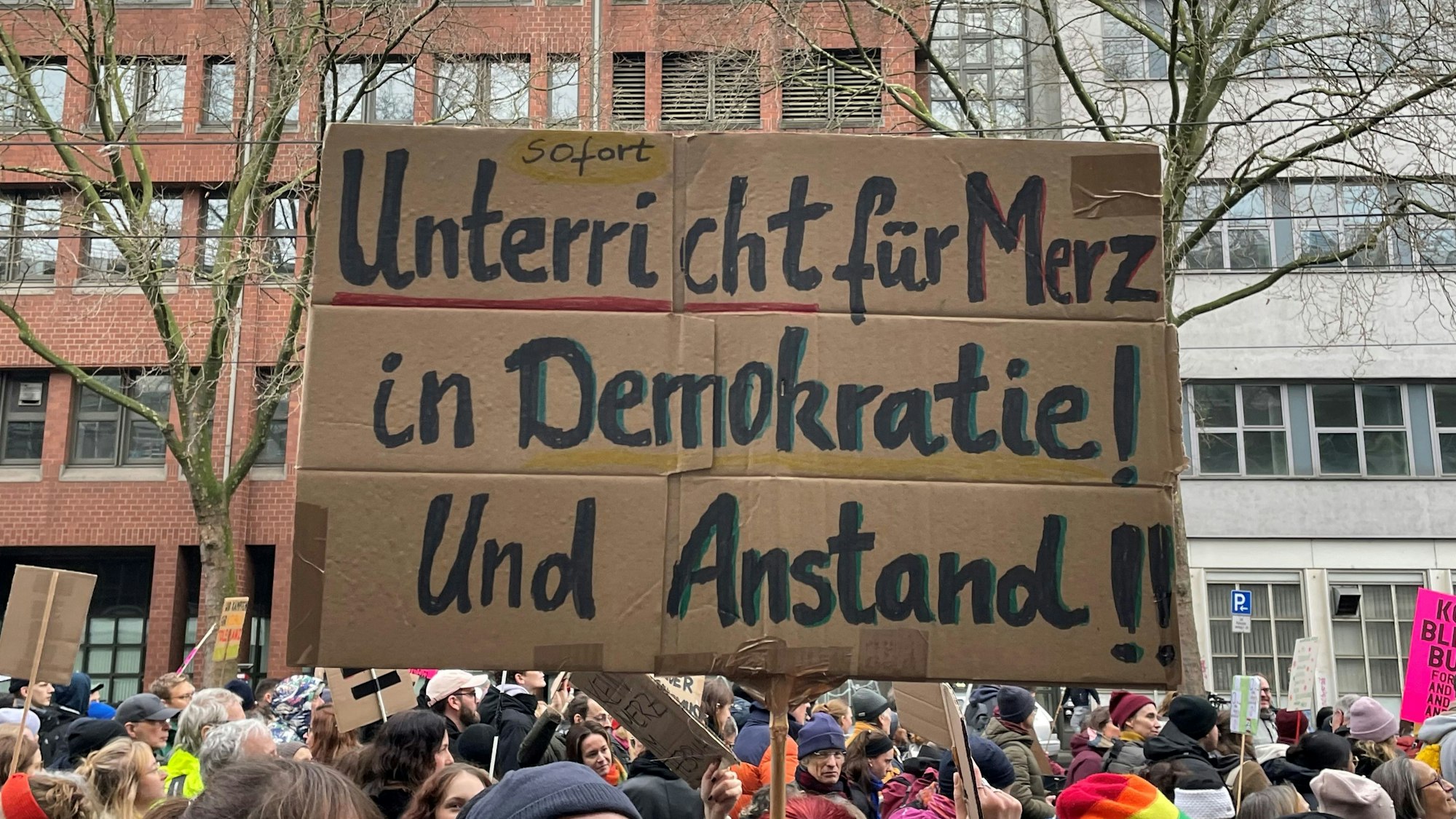 Bei einer Demonstration gegen Rechts in Köln zeigen Teilnehmer ein Plakat mit der Aufschrift „Sofort Unterricht für Merz in Demokratie und Anstand“.