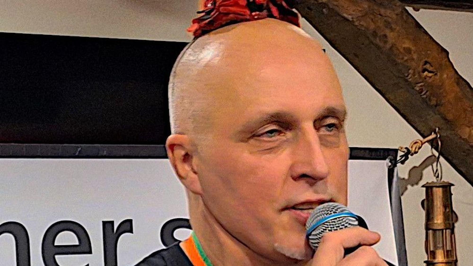 Harald von Bonn spricht in ein Mikrofon. Er trägt ein jeckes Hütchen.