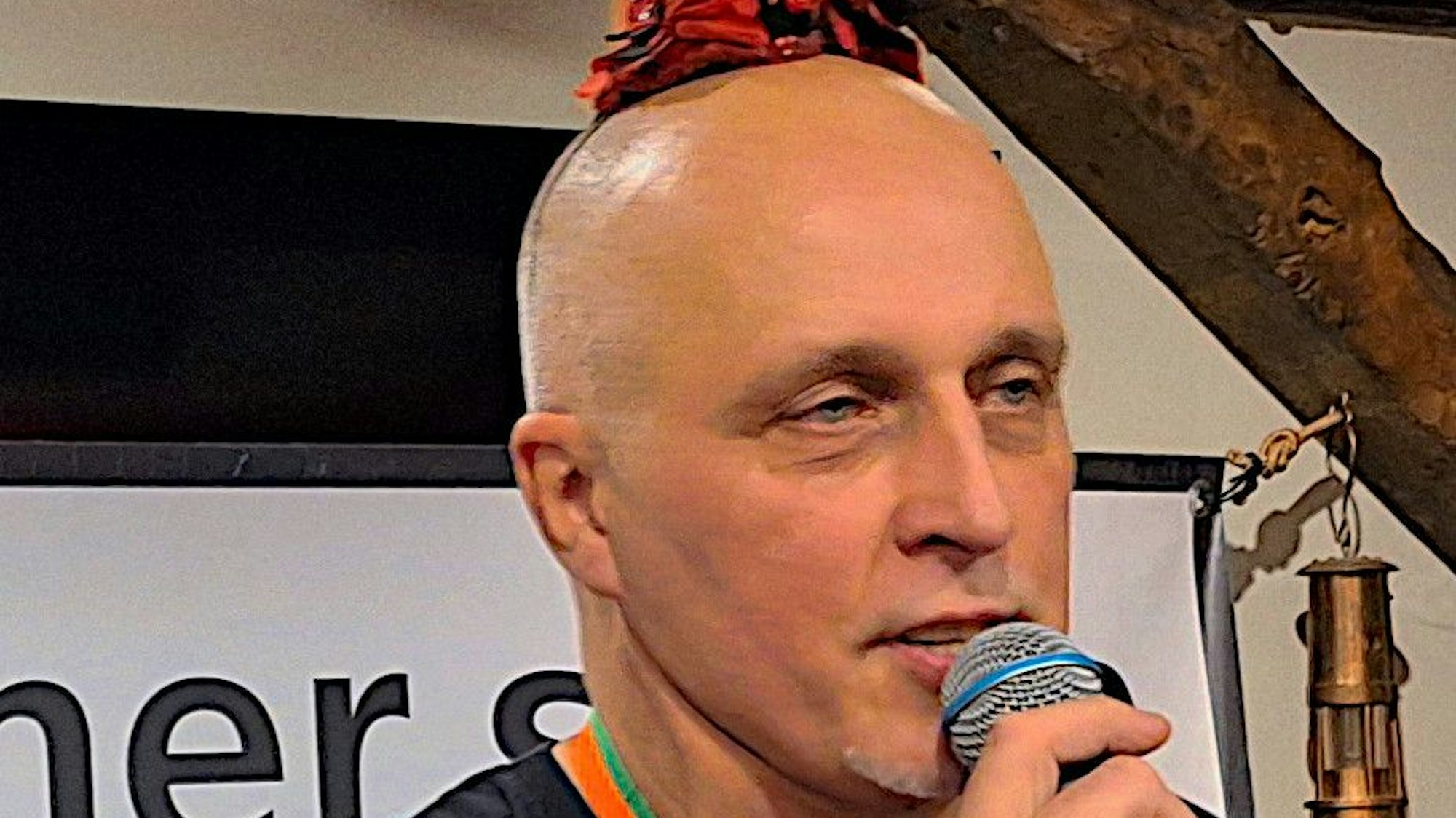 Harald von Bonn spricht in ein Mikrofon. Er trägt ein jeckes Hütchen.