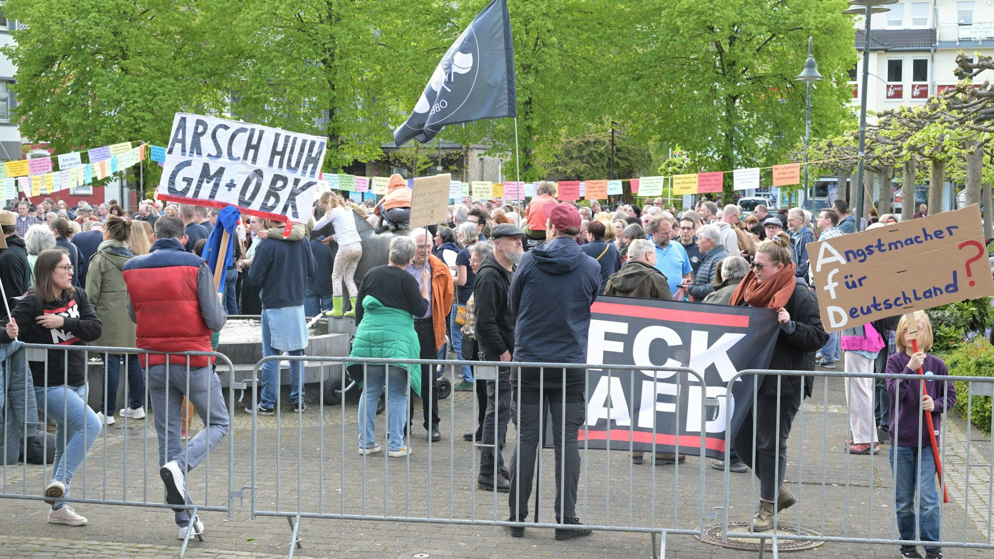 Eine Menschenmenge hat sich hinter einem Zaun versammelt und einige Menschen halten Schilder hoch.