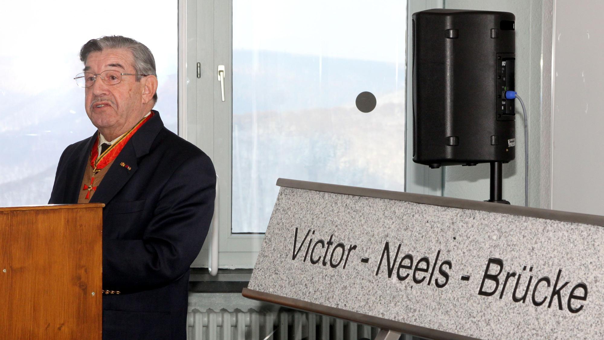 Victor Neels steht vor einem Schild, auf dem Victor-Neels-Brücke steht.