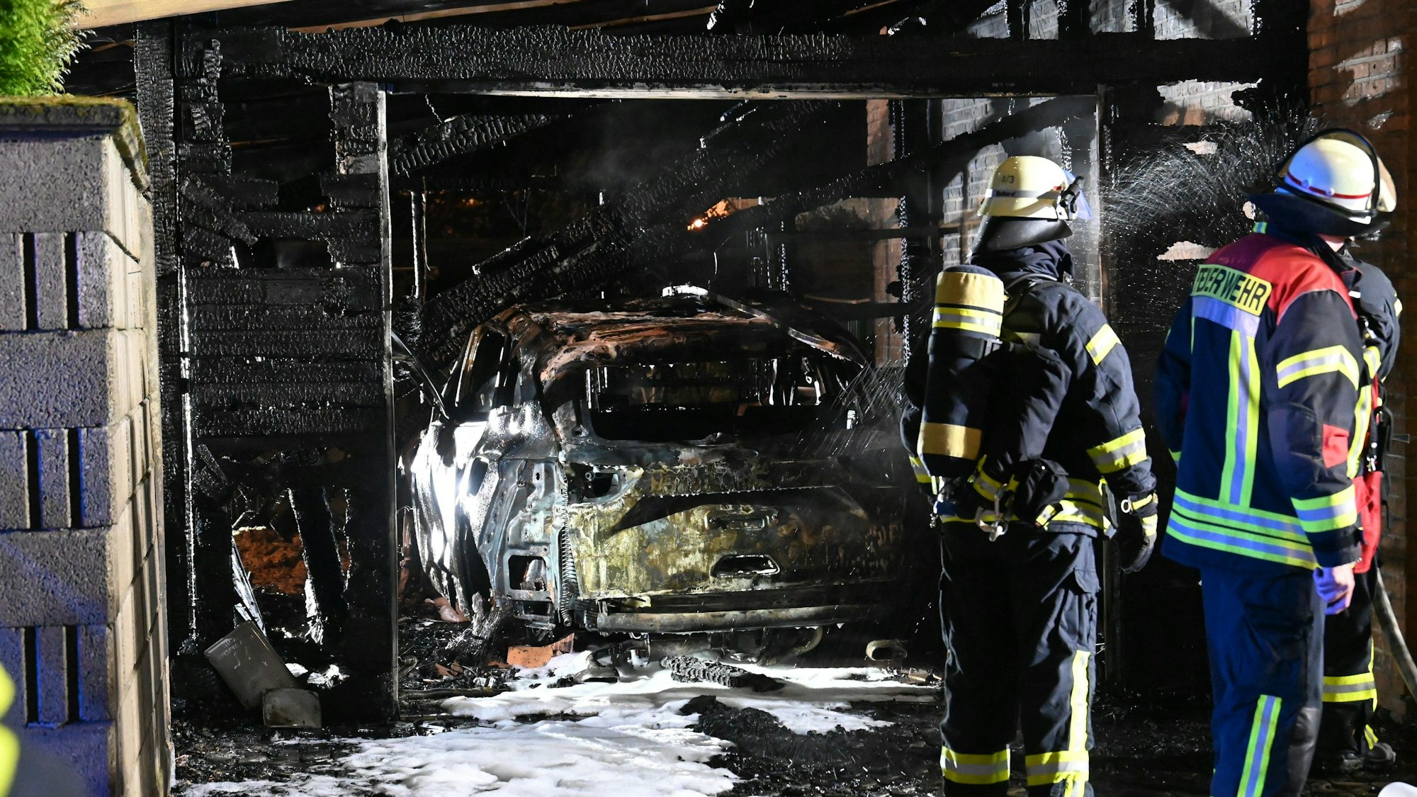 Eine abgebrannte Garage mit einem zerstörten Auto. Am Auto und auf dem Boden sind noch Reste des Löschschaums zu sehen.