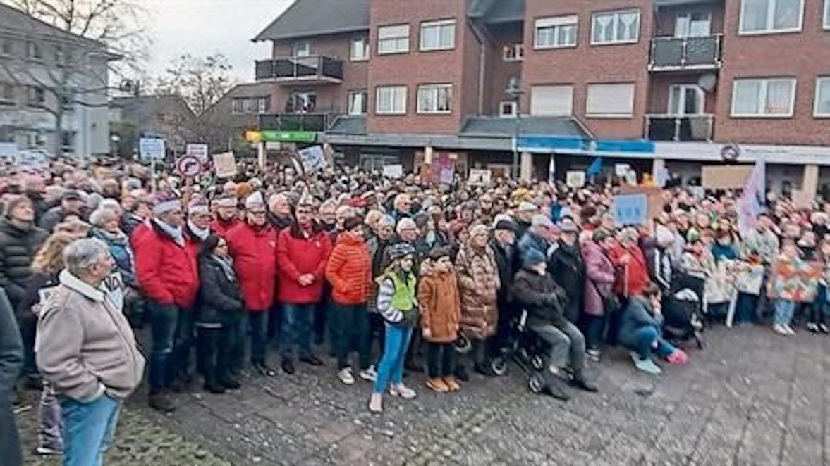 Menschen stehen auf einem Platz. Einige tragen Protestschilder.
