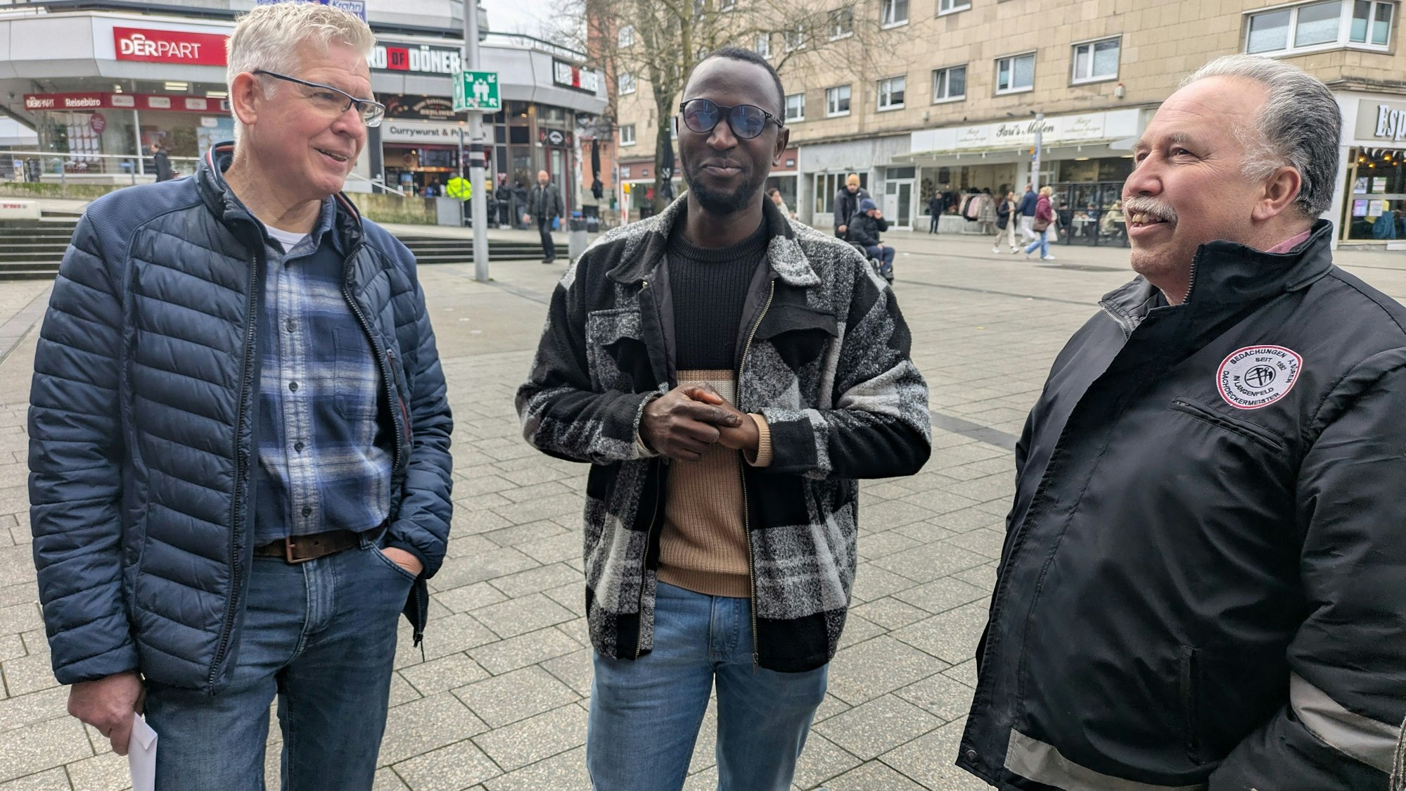 Drei Männer stehen auf einem Platz in Wiesdorf.