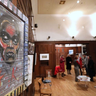 Ein großformatiges Porträt, im Hintergrund weitere Kunstwerke und Menschen, die sie betrachten.