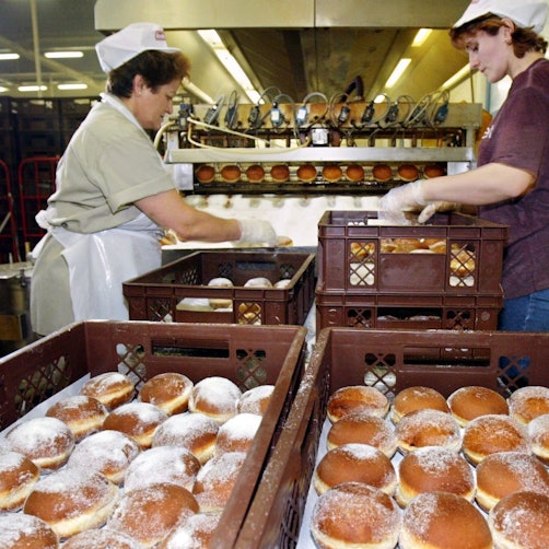 Zwei Arbeiterinnen packen in der Glockenbrot-Bäckerei in Frankfurt frisch gebackene Berliner in Kisten.