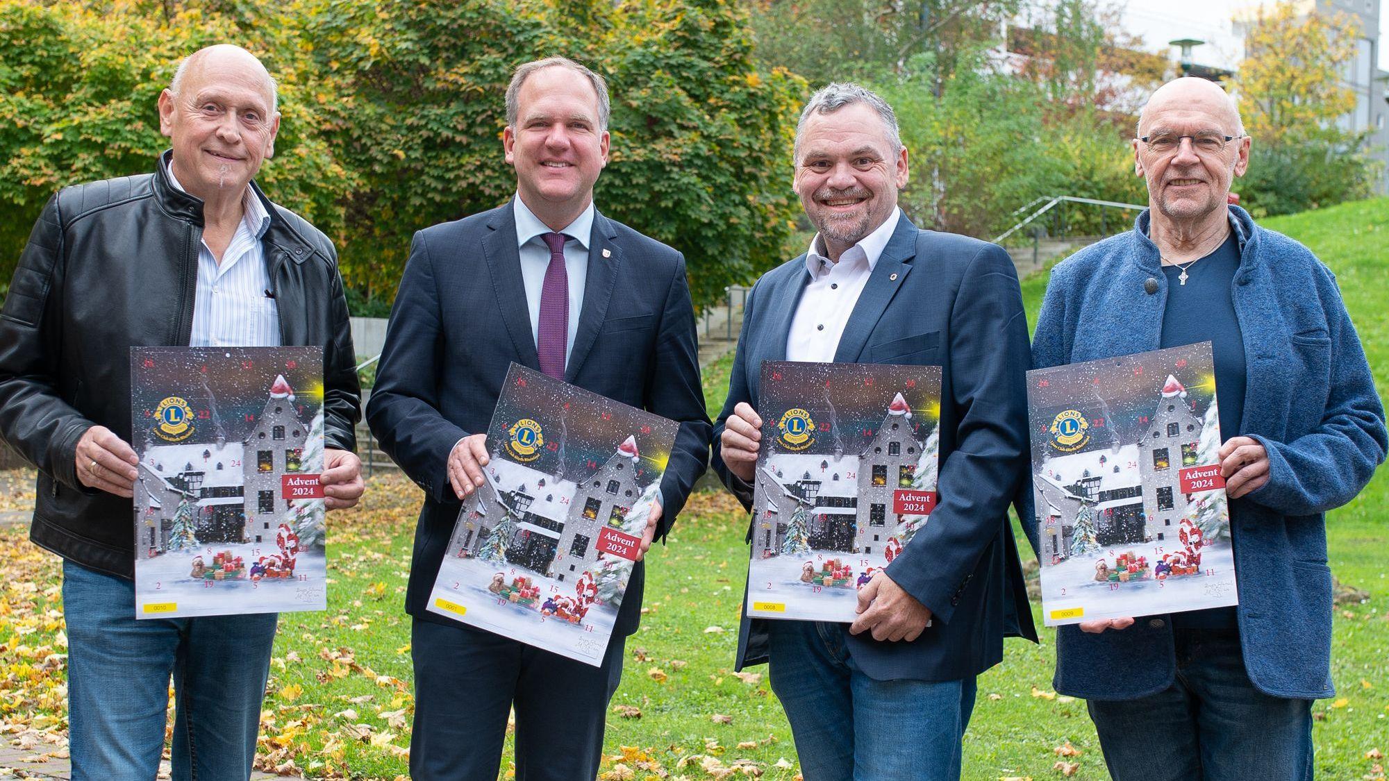 Vier Männer lächeln in die Kamera, jeder hält einen Adventskalender in der Hand.