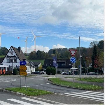 Fotocollage: Ein Kreisverkehr, dahinter ein Fachwerkhaus, am Horizont drei Windräder.