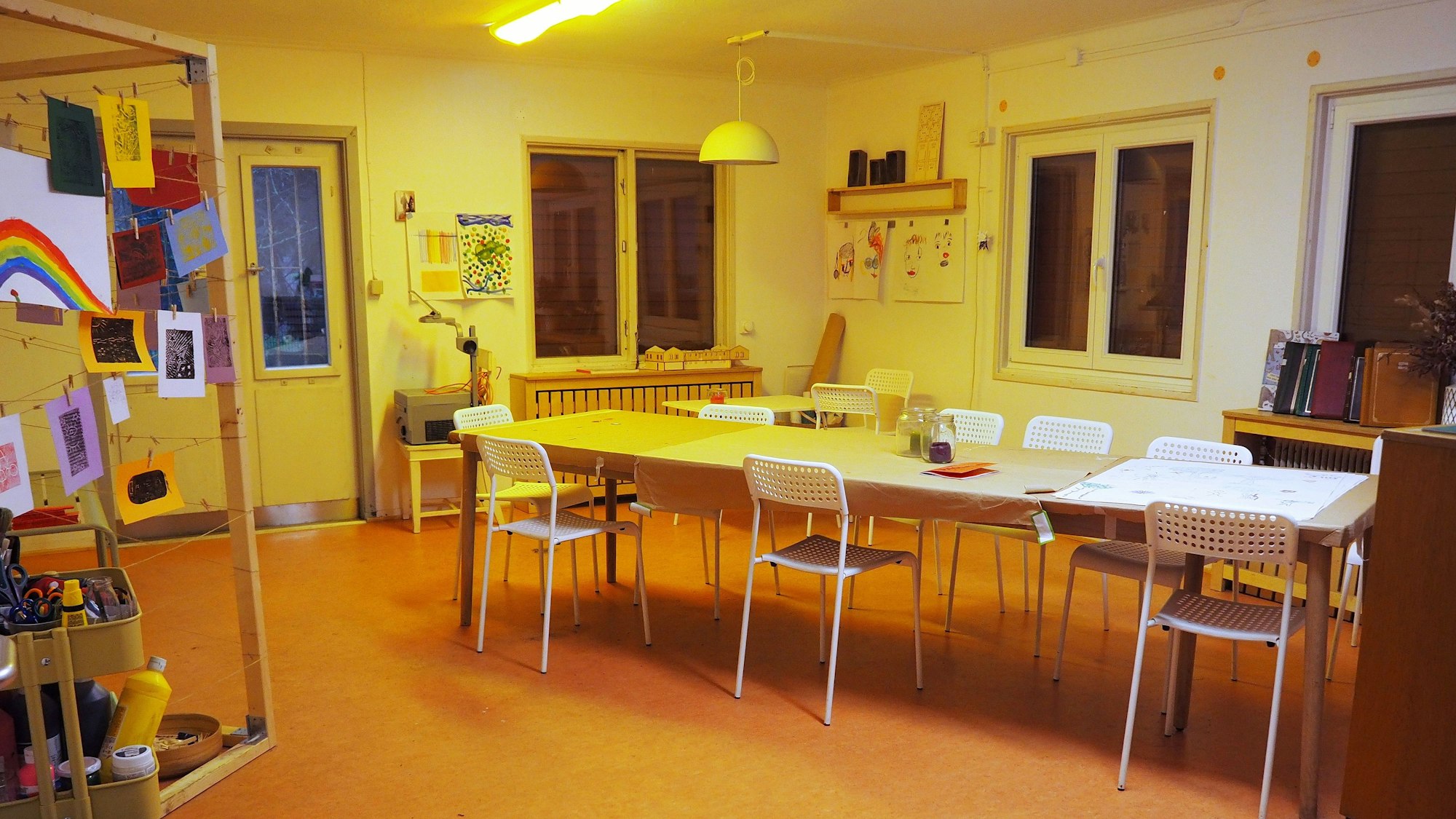 In einem großen Raum steht ein Tisch mit mehreren Stühlen, Bilder hängen an der Wand.