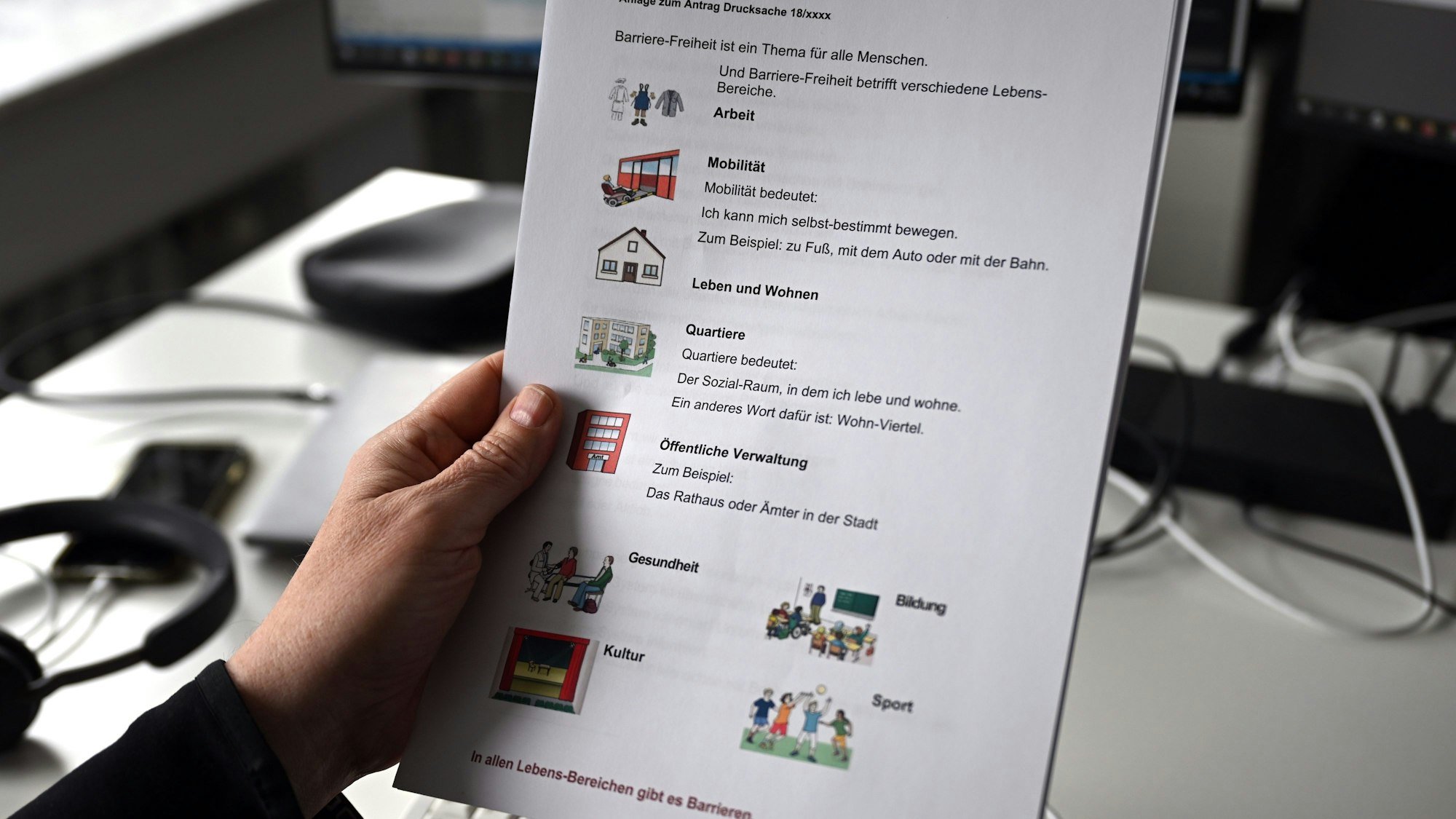 Ein Mann hält im Düsseldorfer Landtag einen Antrag in Leichter Sprache mit Pictogrammen in der Hand.