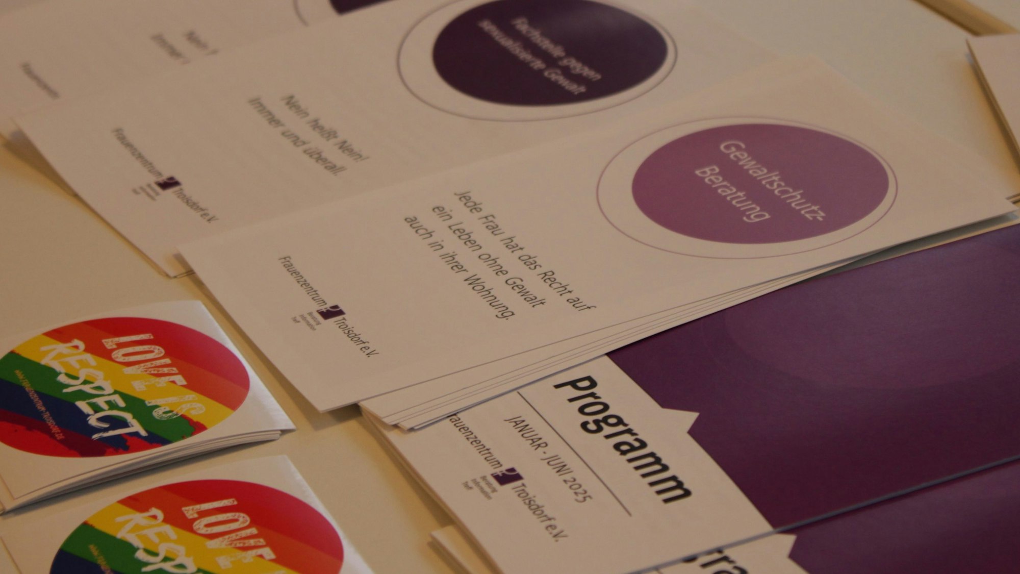 Mehrere Flyer des Troisdorfer Frauenzentrums liegen nebeneinander, auf einem steht "Gewaltschutz-Beratung: Jede Frau hat das Recht auf ein Leben ohne Gewalt auch in ihrer Wohnung".