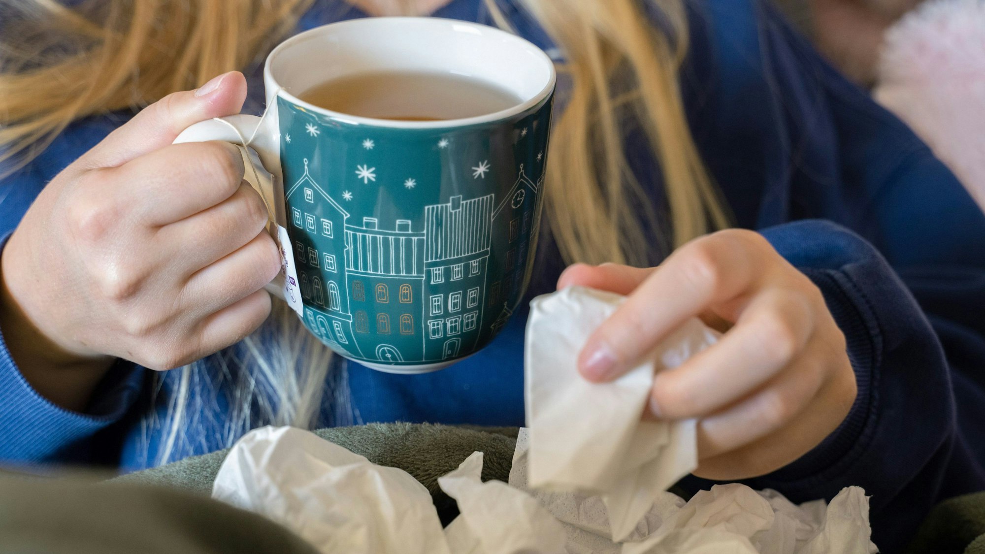Eine Person trinkt Tee und hält ein Taschentuch in ihrer Hand. (Symbolfoto)