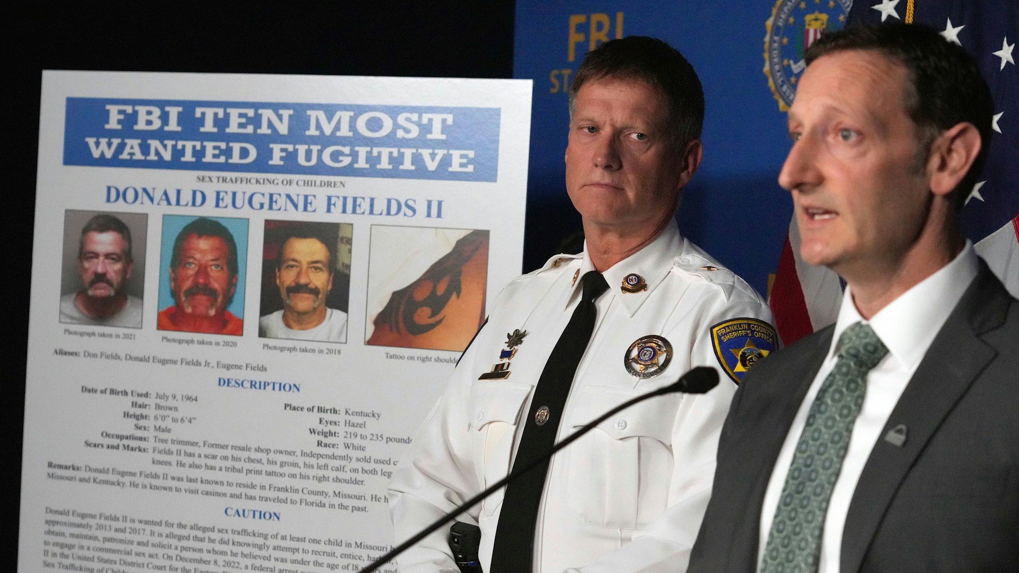 Franklin County Sheriff Steven Pelton steht in der Nähe eines Posters von Donald Eugene Fields II, während der leitende FBI-Sonderagent des St. Louis-Büros, Jay Greenberg, am 25. Mai 2023, in St. Louis über die Aufnahme von Fields in die Liste der zehn meistgesuchten Flüchtigen des FBI spricht.