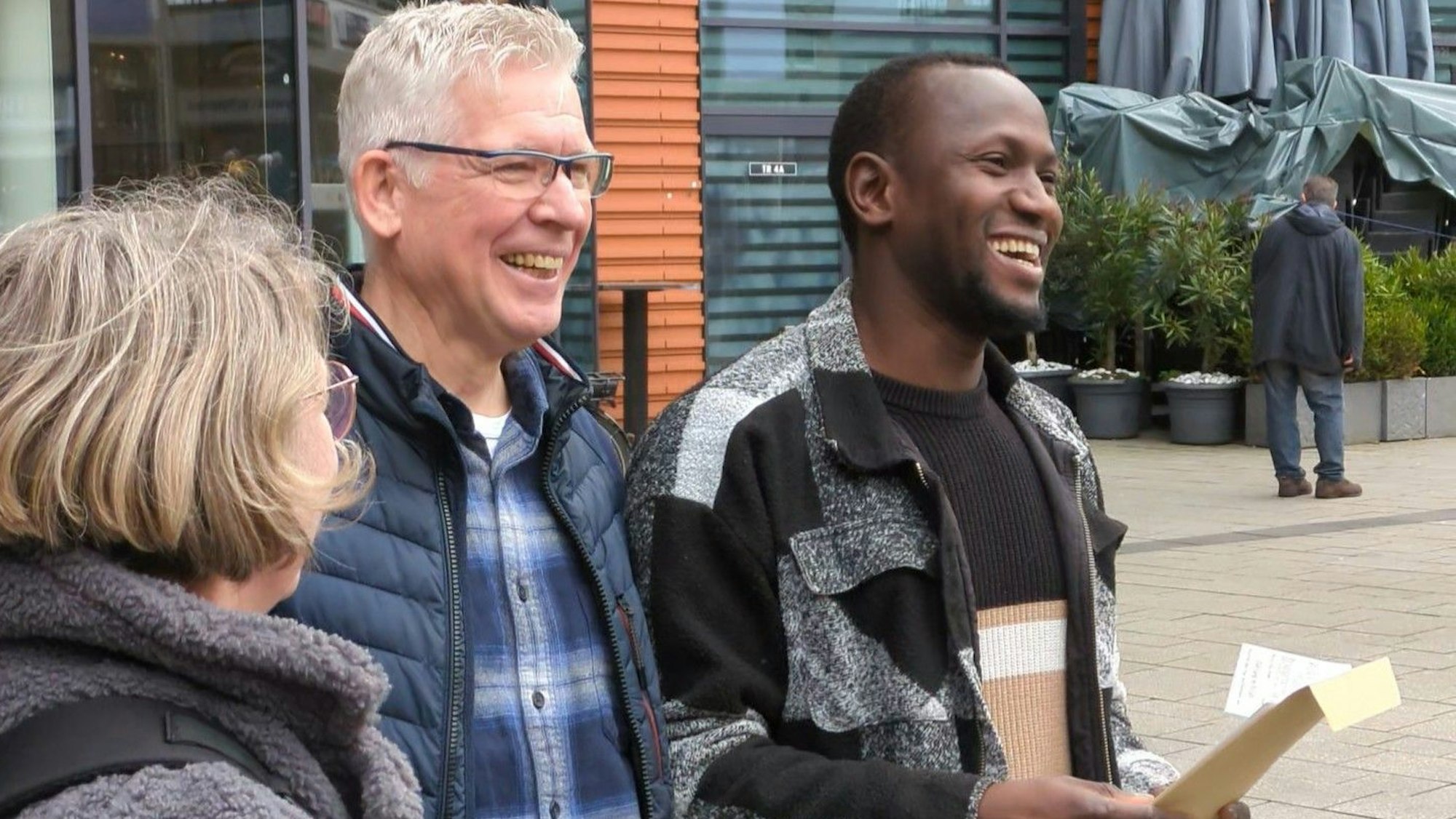 Drei Menschen freuen sich auf einem Platz.