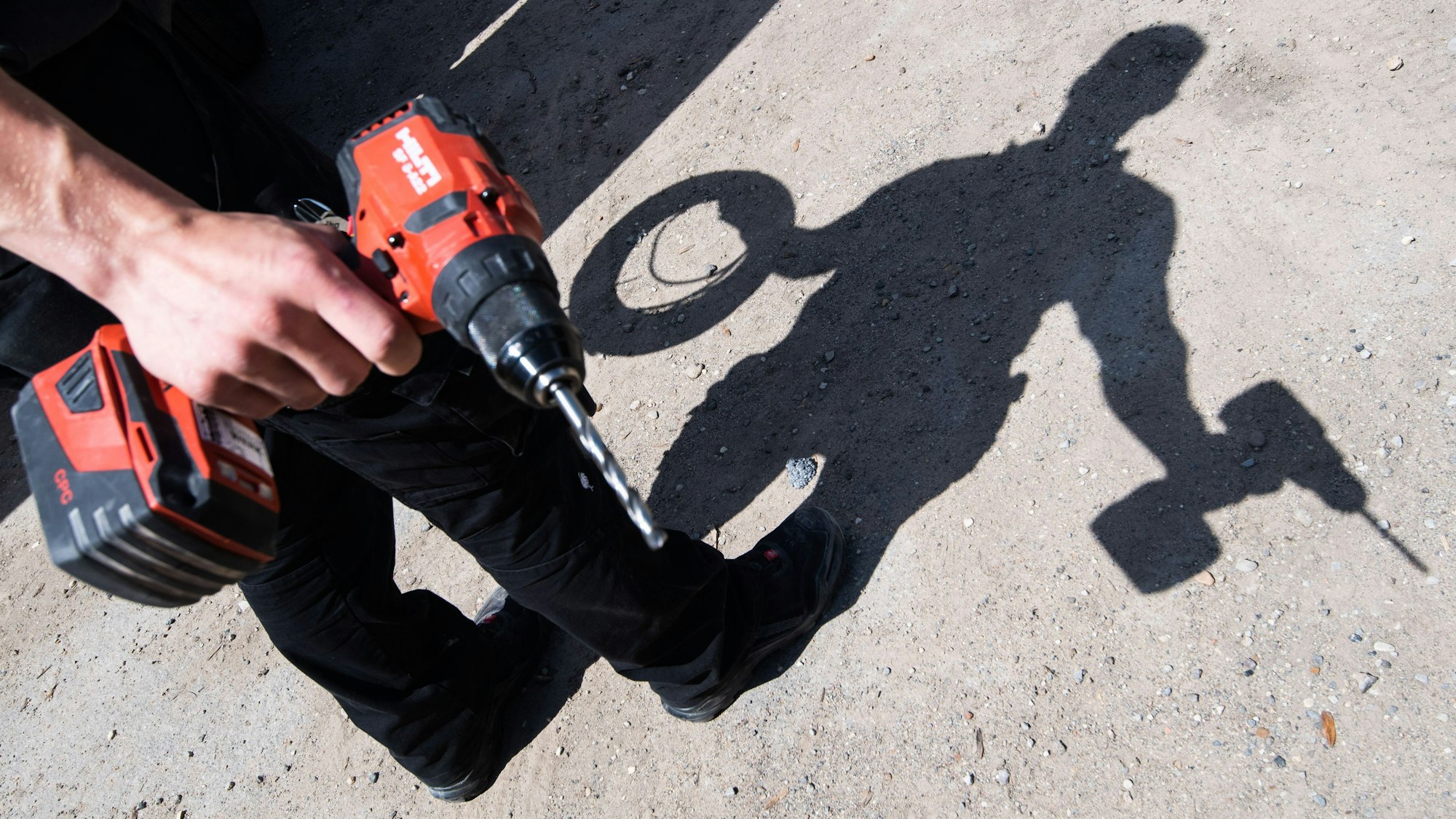 Ein Auszubildender eines Elektroinstallationsbetriebes wirft mit aufgerollten Kabel und einem Akkuschrauber einen Schatten.