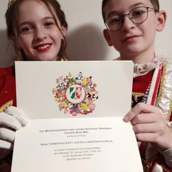 Das Kaller Kinderprinzenpaar Prinz Emil (Sträußl) und Prinzessin Annika (Pleuß) hält eine Einladung zum Empfang von Ministerpräsident Hendrik Wüst in den Händen.