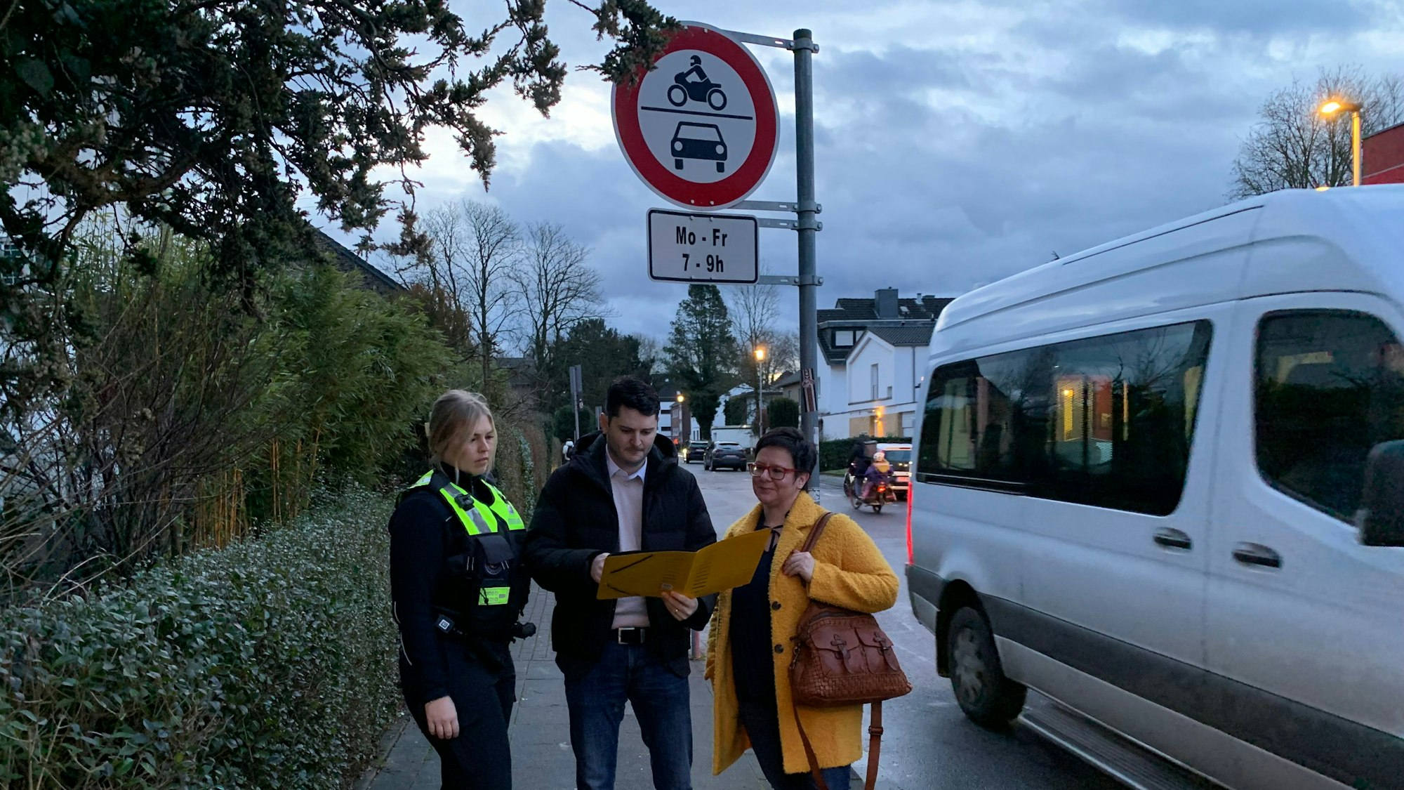 Drei Personen stehen an der Einmündung einer Straße und schauen in eine aufgeschlagene Mappe.