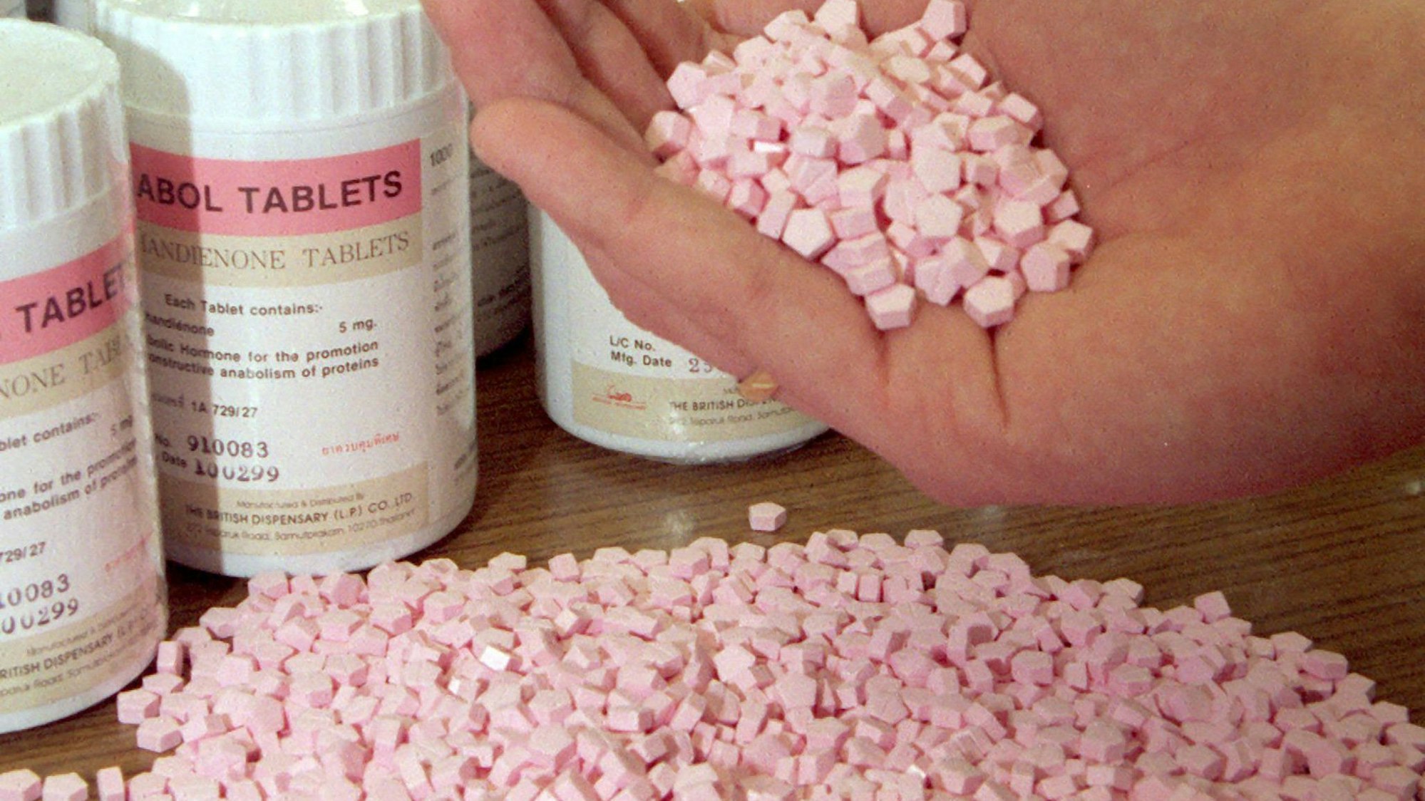 Pillen zum Muskelaufbau befinden sich auf einem Tisch und in einer Hand