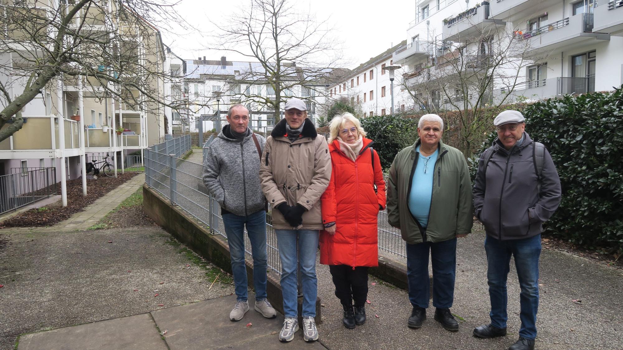 Vier Männer und eine Frau stehen im Hof einer Wohnanlage mit vielen mehrgeschossigen Gebäuden.