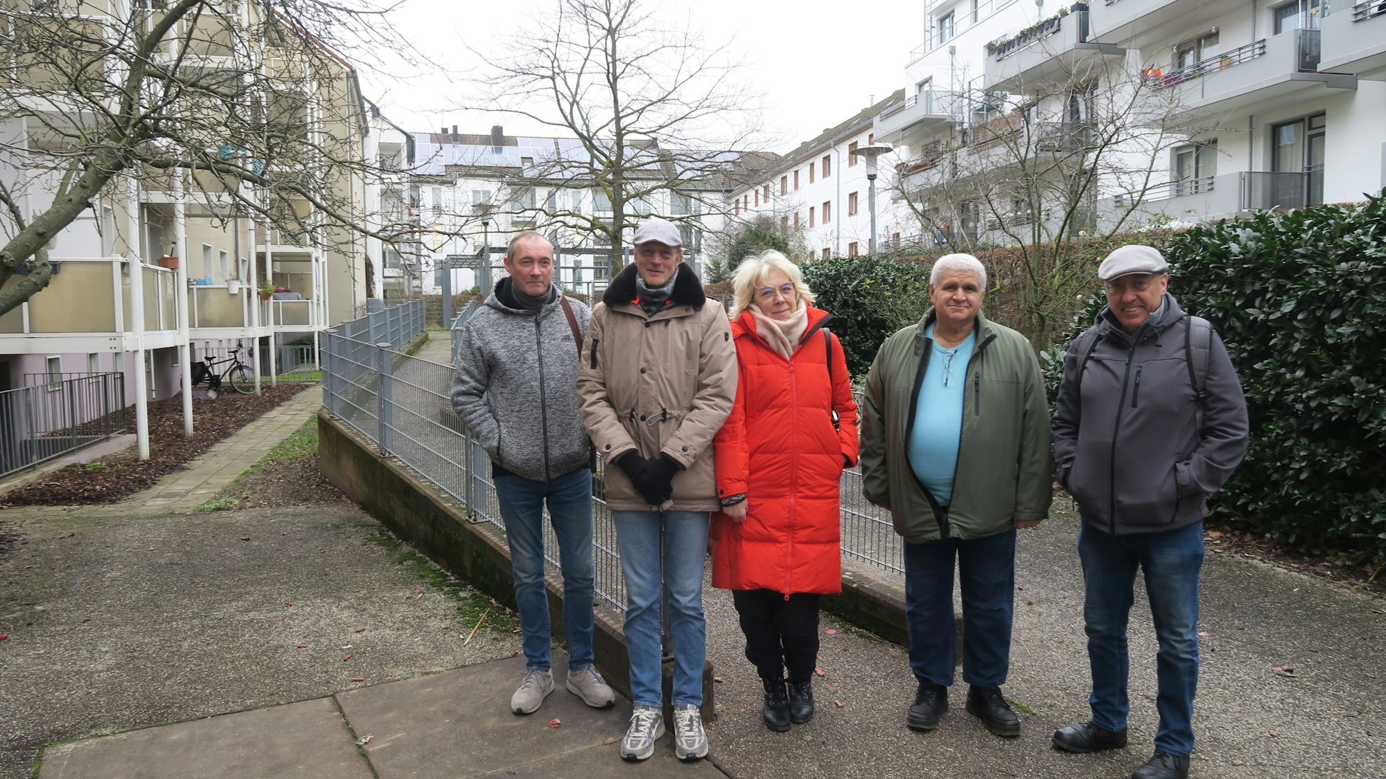 Vier Männer und eine Frau stehen im Hof einer Wohnanlage mit vielen mehrgeschossigen Gebäuden.