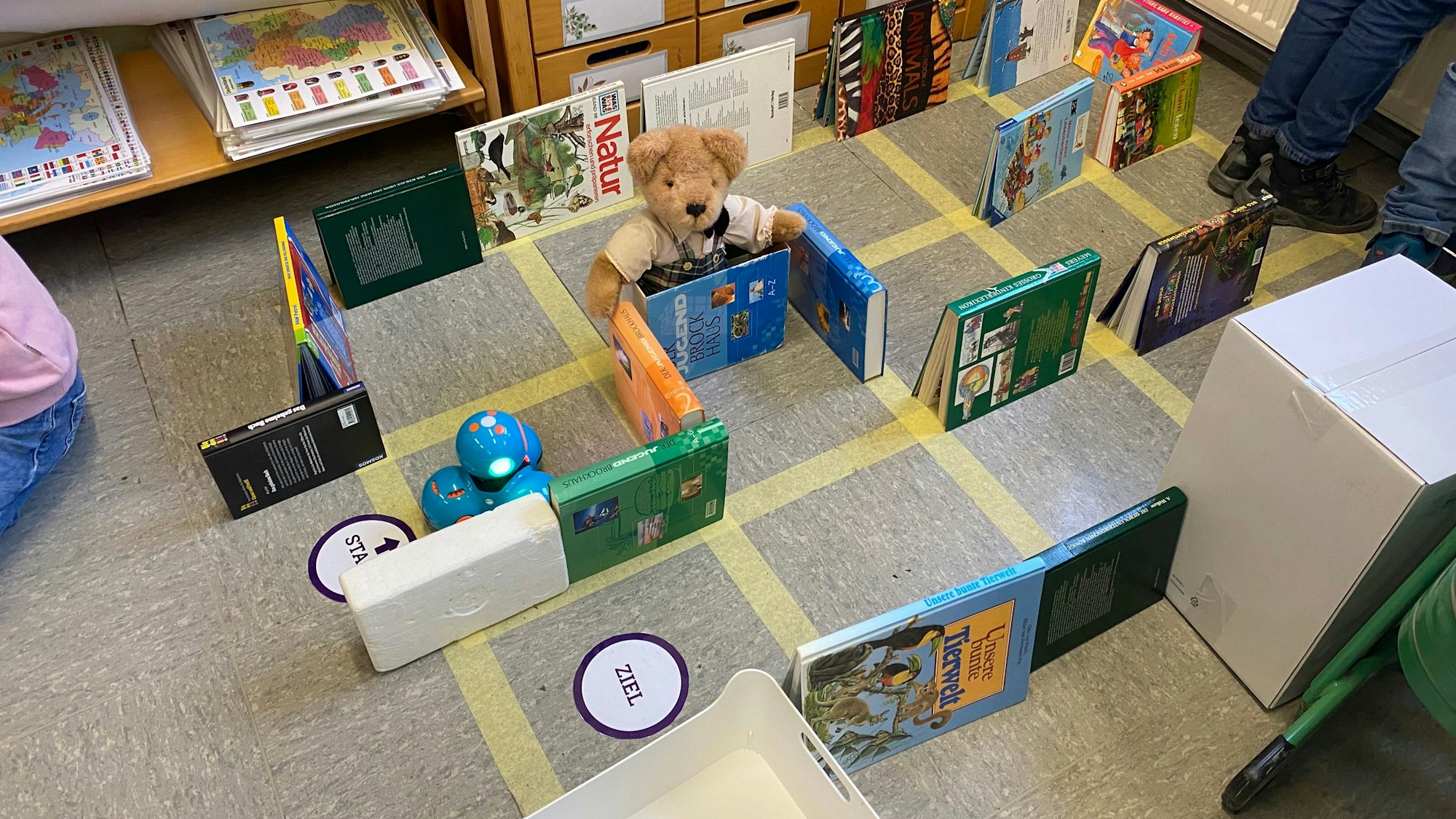 Ein mit Bücher aufgebauter Parcours auf einem aufgeklebten Gitternetz mit einem blauen, aus vier Kugeln bestehenden Roboter