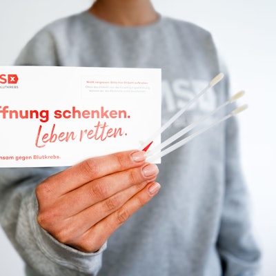 Das Foto zeigt eine Hand mit drei Wattestäbchen und einem Testset der DKMS.