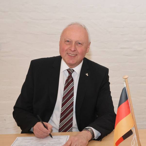 Portraitfoto von Gero Karthaus, er schaut direkt in die Kamera und trägt einen dunklen Anzug, weißes Hemd und Krawatte.
