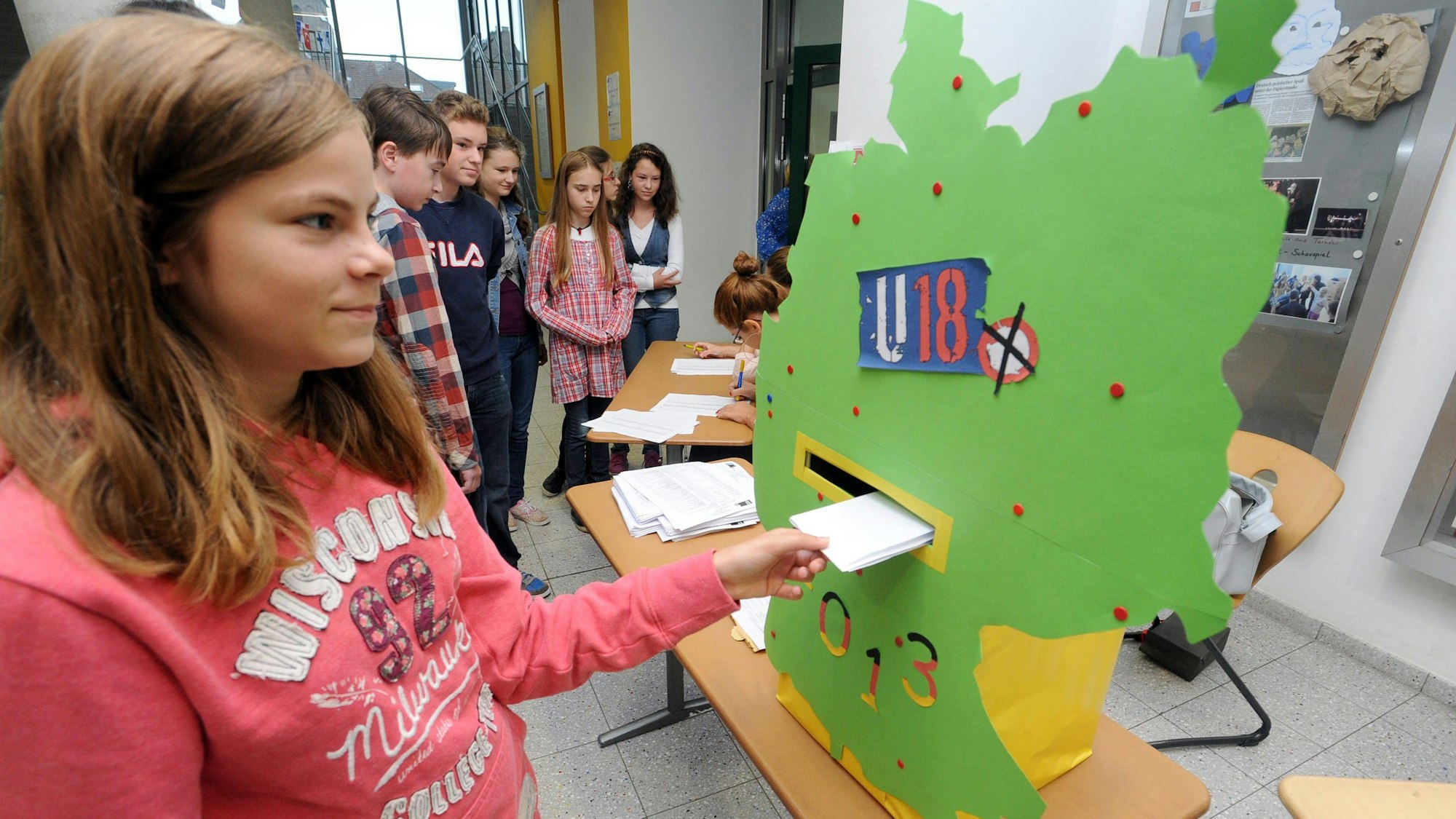 Ein Mädchen wirft einen Wahlzettel in eine bunte Wahlurne.