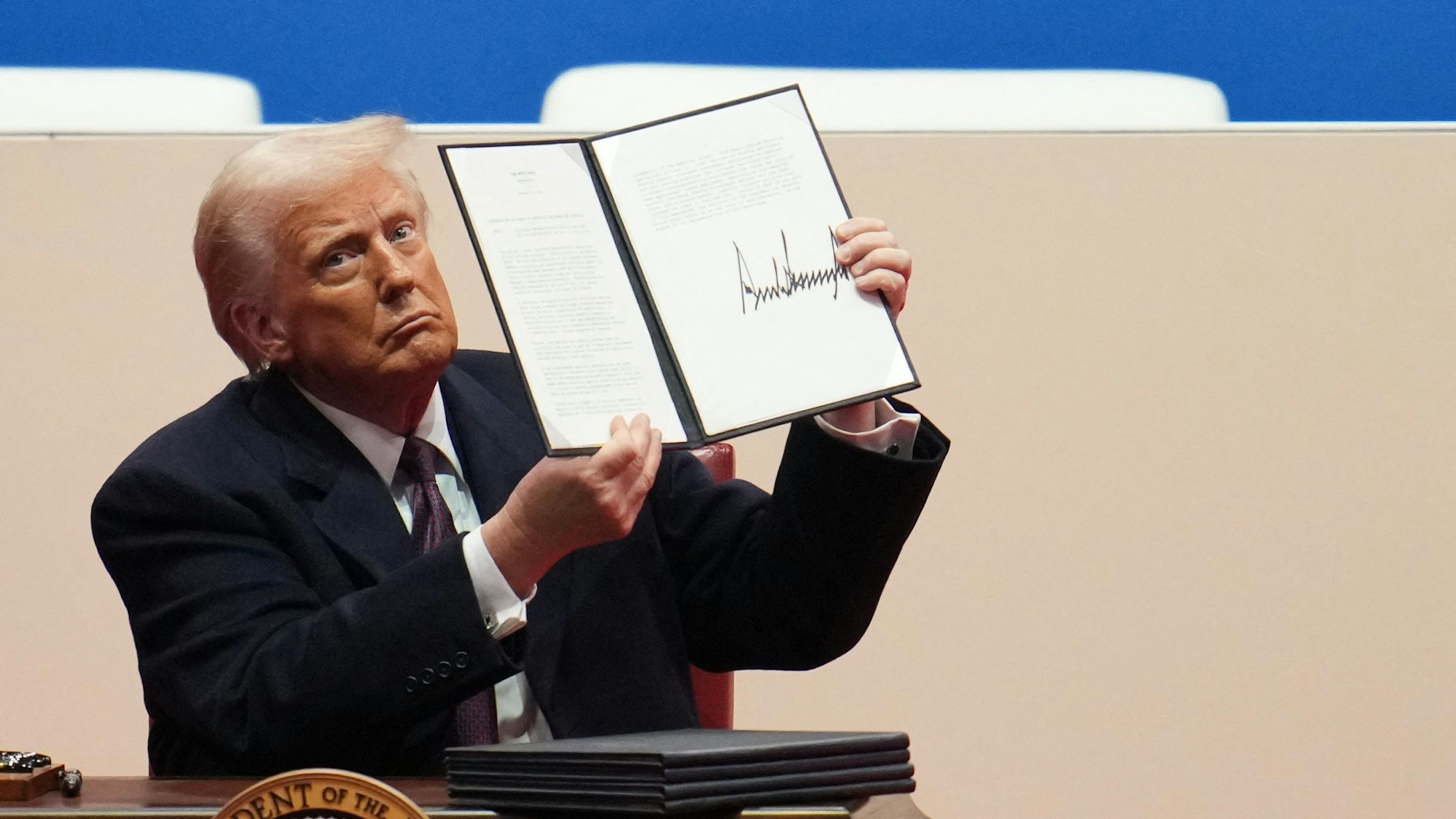 Donald Trump hält ein Dekret mit seiner Unterschrift in die Höhe.