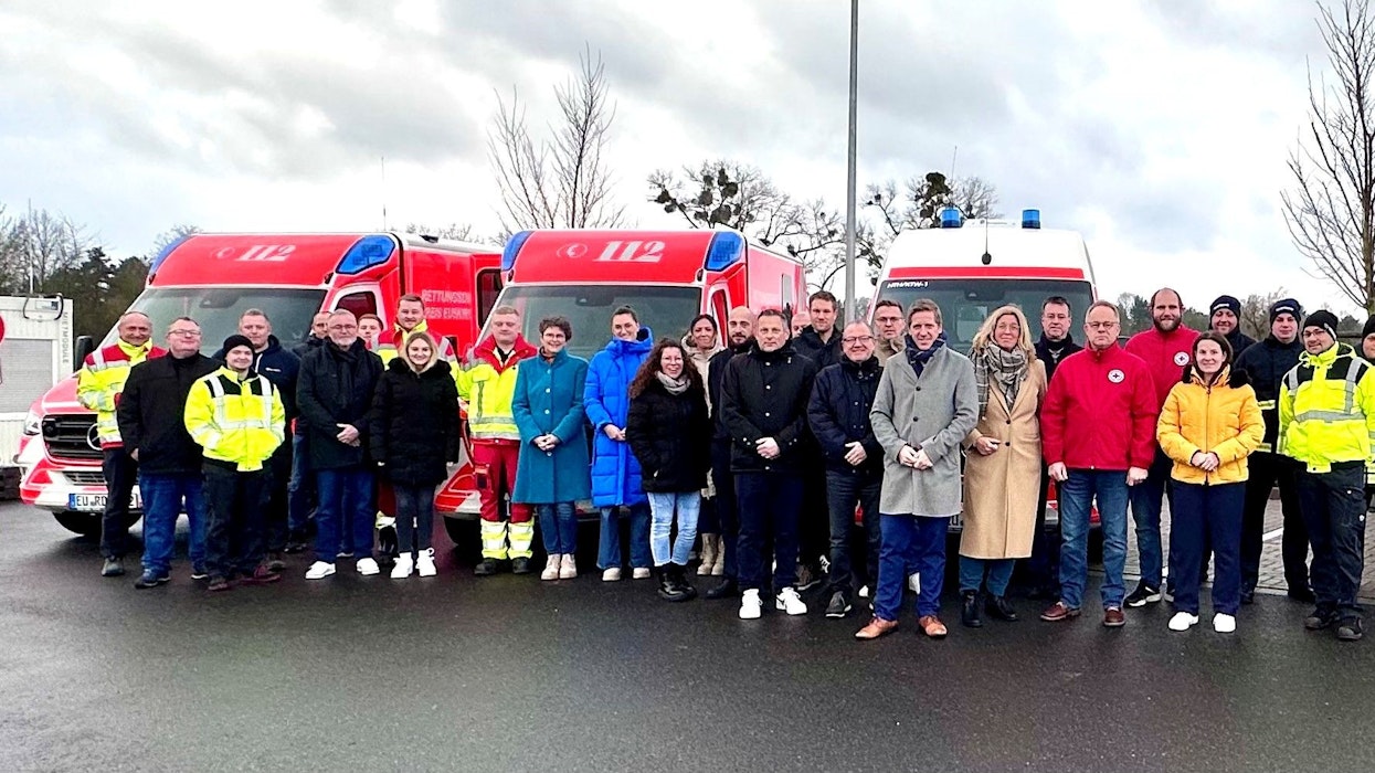 Eine große Gruppe Menschen steht vor drei Einsatzfahrzeugen der Rettungswache.