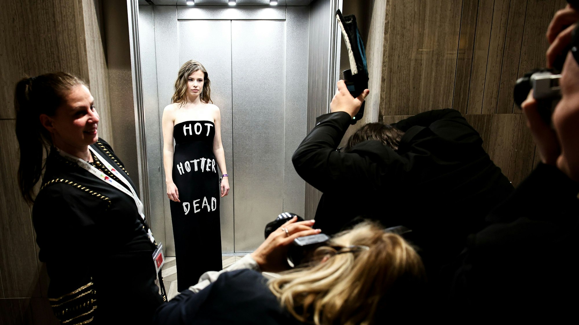 Klimaaktivistin Luisa Neubauer wird von Fotografen in einem Aufzug fotografiert. Auf ihrem Kleid steht „Hot Hotter Dead“.