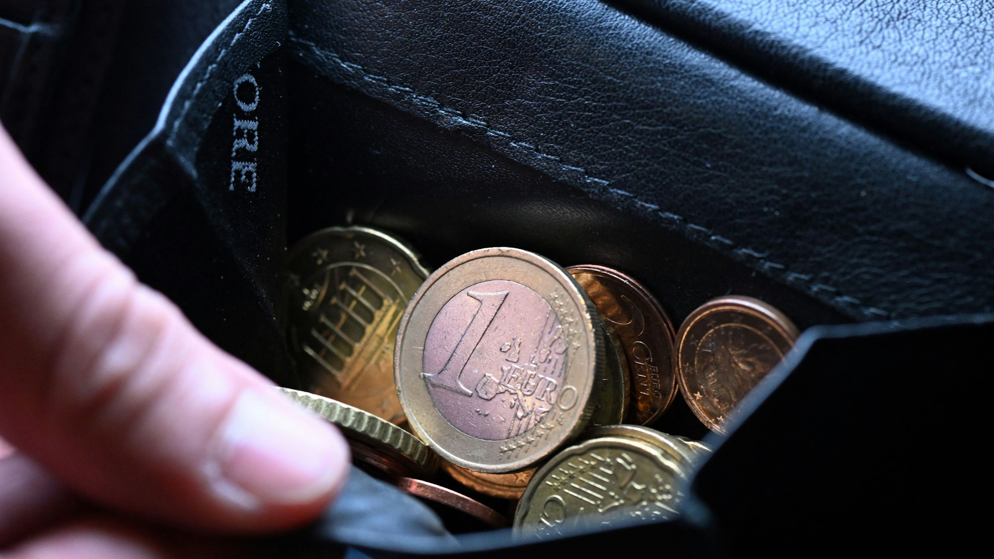 Eine Hand greift in einen Geldbeutel mit Münzen.