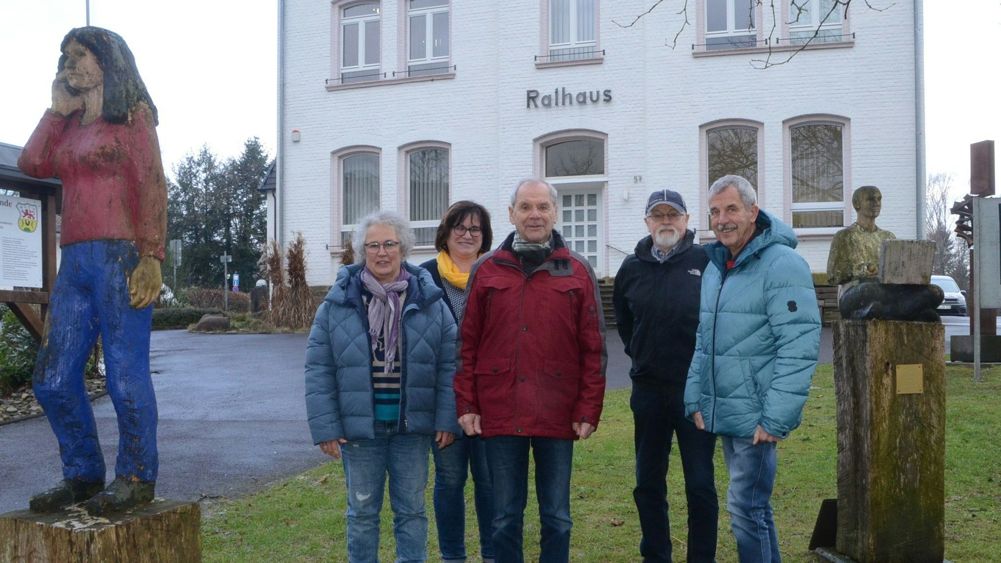 Männer und Frauen stehen vor einem weißen Gebäude mit der Schrift "Rathaus" über der Eingangstür. Links und rechts der Gruppe stehen Skulpturen auf Sockeln.