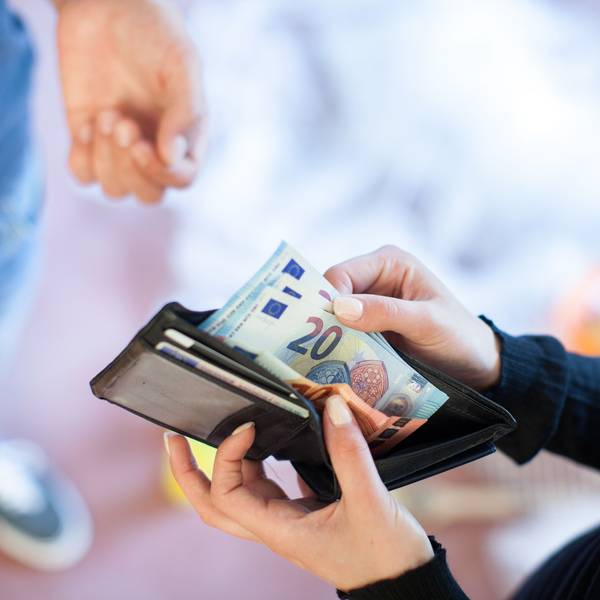 Eine Person zieht 20-Euro-Scheine aus ihrem Portemonnaie, um sie einer anderen Person zu geben.