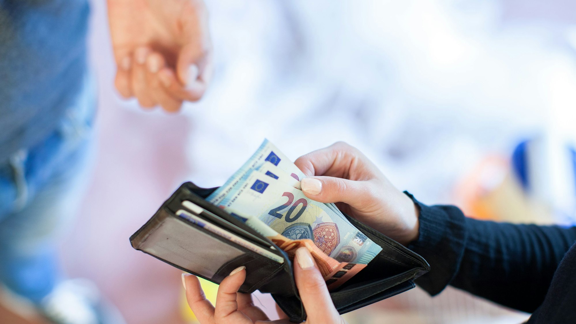Eine Person zieht 20-Euro-Scheine aus ihrem Portemonnaie, um sie einer anderen Person zu geben.