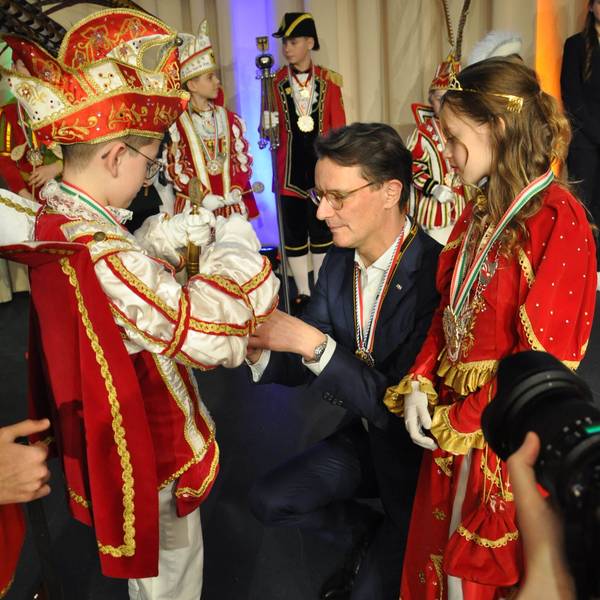 Ministerpräsident Hendrik Wüst kniet vor dem Kinderprinzen aus Kall, der ihm einen Orden umhängt.